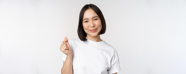 白いbaに対して立っているTシャツを着て指ハートジェスチャーを示して笑っている美しいアジアの女性