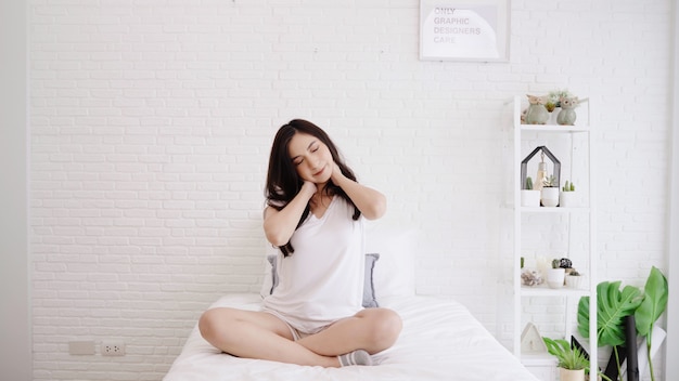 Красивая азиатская женщина протягивая ее тело после того как она просыпает в ее спальне дома.