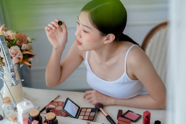 Free photo beautiful asian woman white tshirt smile with happiness hand hold blush on and makeup cosmetic items in bedroom with healthy face skincare concept