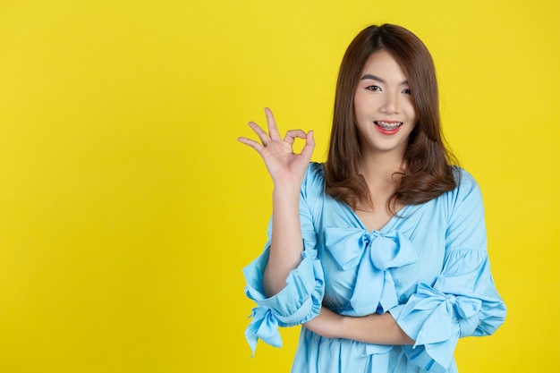 Beautiful asian woman with okey gesture on yellow wall
