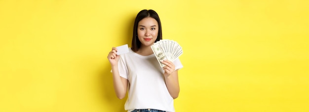 Beautiful asian woman with short dark hair wearing white tshirt showing money in dollars and plastic