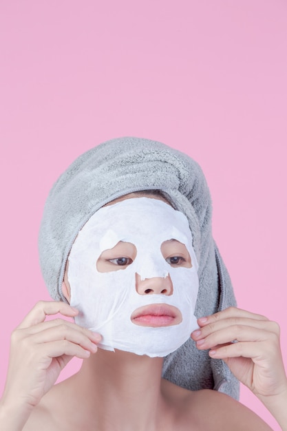 Красивые азиатские женщины используют лицо маски на листе на розовом фоне.