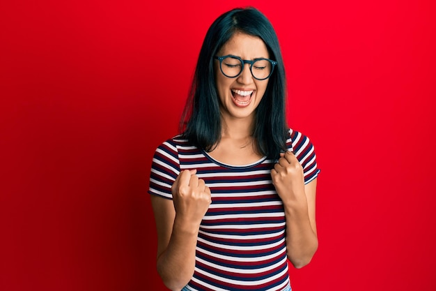 Free photo beautiful asian young woman wearing casual clothes and glasses celebrating surprised and amazed for success with arms raised and eyes closed