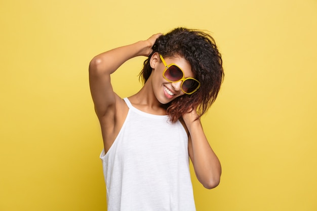 Beautiful attractive African American woman posting play with her curly afro hair. Yellow studio background. Copy Space.