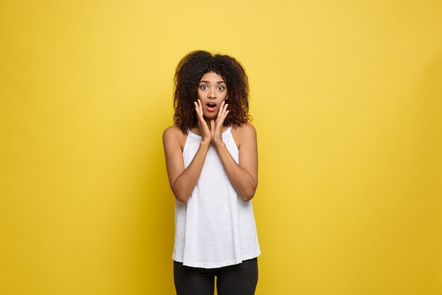 Beautiful attractive African American woman posting play with her curly afro hair. Yellow studio background. Copy Space.