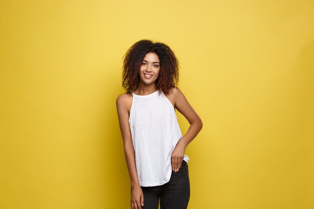 Beautiful attractive African American woman posting play with her curly afro hair. Yellow studio background. Copy Space.