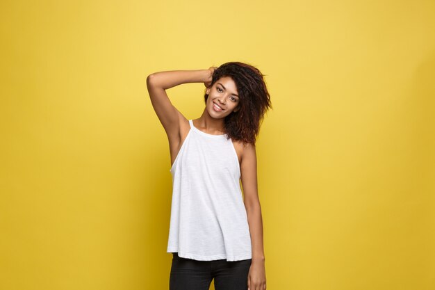 Bella attraente donna afroamericana postando giocare con i capelli ricci afro. sfondo di studio giallo. copia spazio.