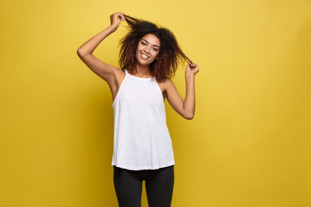 Beautiful attractive African American woman posting play with her curly afro hair. Yellow studio background. Copy Space.