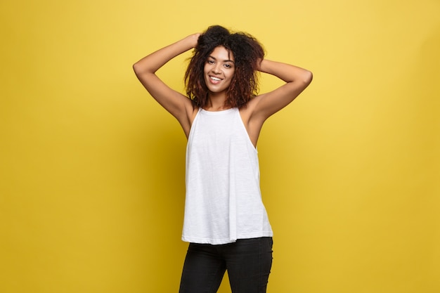 Beautiful attractive African American woman posting play with her curly afro hair. Yellow studio background. Copy Space.