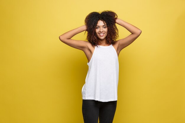 Beautiful attractive African American woman posting play with her curly afro hair. Yellow studio background. Copy Space.