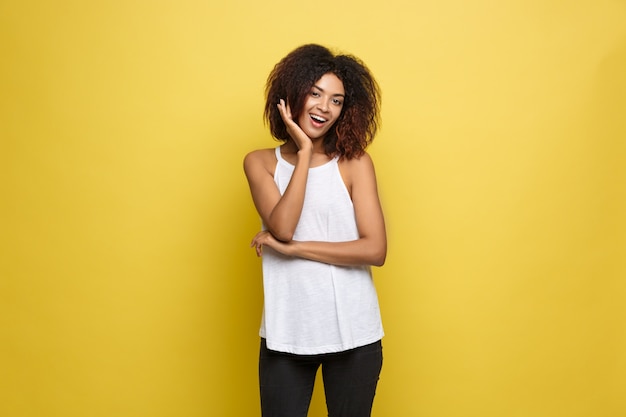 Beautiful attractive African American woman posting play with her curly afro hair. Yellow studio background. Copy Space.