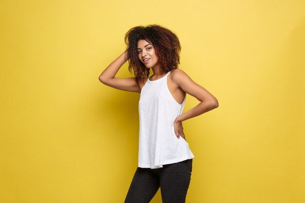 Beautiful attractive African American woman posting play with her curly afro hair. Yellow studio background. Copy Space.