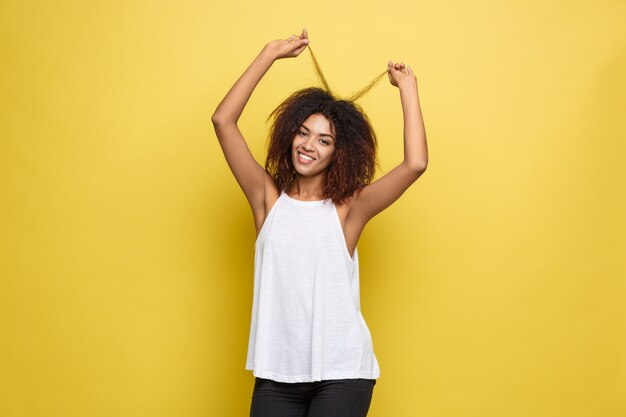 Beautiful attractive African American woman posting play with her curly afro hair. Yellow studio background. Copy Space.