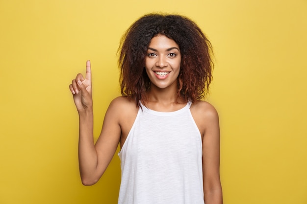 Beautiful attractive African American woman posting play with her curly afro hair. Yellow studio background. Copy Space.