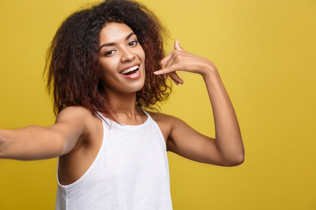 Beautiful attractive African American woman posting play with her curly afro hair. Yellow studio background. Copy Space.