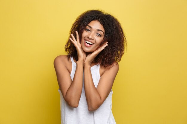 Beautiful attractive African American woman posting play with her curly afro hair. Yellow studio background. Copy Space.