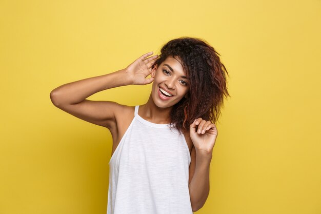 Beautiful attractive African American woman posting play with her curly afro hair. Yellow studio background. Copy Space.