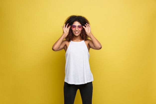 Beautiful attractive African American woman with trendy glasses posting over yellow studio background. Copy Space.