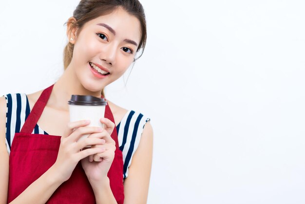 아름다운 매력적인 아시아 여성 커피숍 주인은 앞치마 캐주얼 드레스를 입고 자신감 있고 쾌활한 환영을 받으며 흰색 배경을 격리하는 커피 딩크 미소를 손에 들고 있습니다.