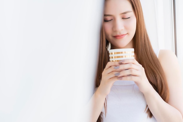 Beautiful attractive asian girl white tshirt enjoy weekend vacation with hot drink in white interior room background