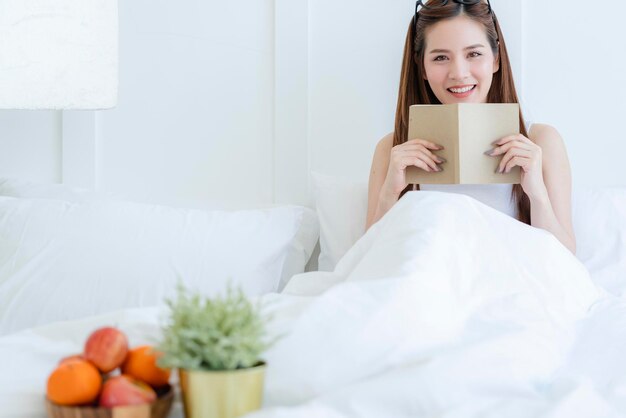 Beautiful attractive asian woman enjoy reading book on bed portrait of asian long hair woman enjoy weekend activity white bedroom