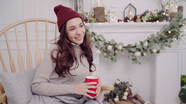 Beautiful attractive Asian woman holding a warm cup of coffee or tea while lying on chair 