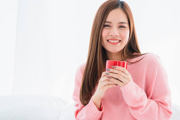 Beautiful attractive asian woman pink sweater with hot drink on white bed morning freshness healthy lifestyle