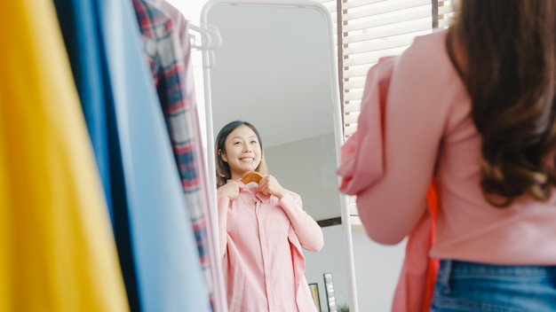 Beautiful attractive lady choosing clothes on clothes rack dressing looking herself in mirror in bedroom at house.