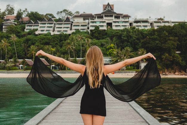 Foto gratuita bella donna attraente vestita in abito nero in posa sul molo in hotel resort di lusso, vacanze estive, spiaggia tropicale