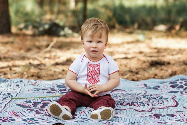 Free photo beautiful baby boy one years old sitting on ground. toddler have fun in spring forest