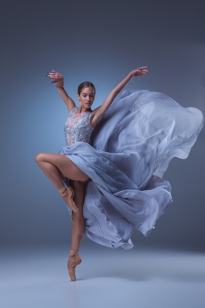 красивая балерина танцует в длинном синем платье на синем фоне