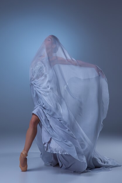 The beautiful ballerina dancing in long blue dress on blue background