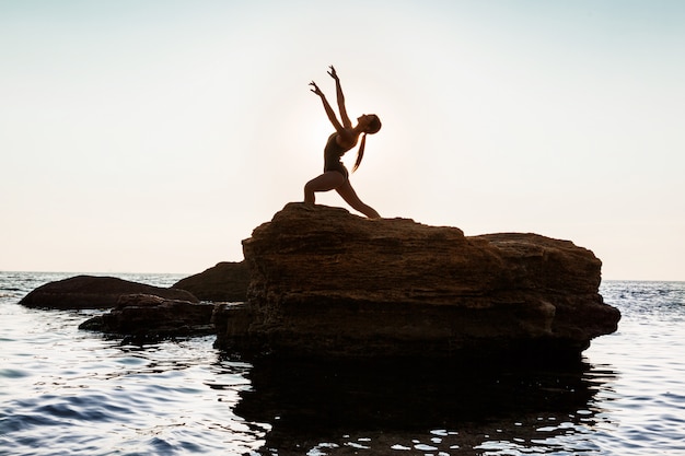 Foto gratuita bella ballerina danza, posa su roccia in spiaggia, vista sul mare.