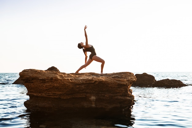 Beautiful ballerina dancing, posing on rock at beach