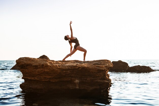 Beautiful ballerina dancing, posing on rock at beach