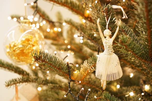 Красивая балерина украшает ветку елки. праздничный фон из зеленой елки и золотых шаров