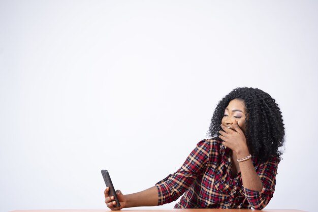 Beautiful black woman sitting at a desk feeling excited while viewing something on her phone