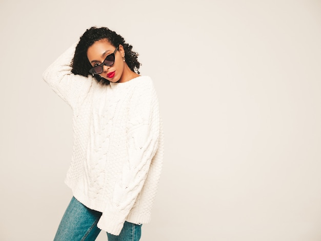 Free photo beautiful black woman with afro curls hairstyle and red lips.smiling model in  trendy jeans clothes and winter sweater.