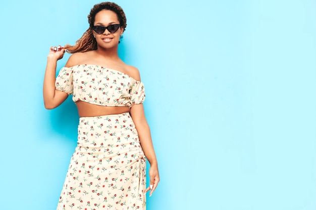 Beautiful black woman with afro curls hairstyle Smiling model dressed in summer dress Sexy carefree female posing near blue wall in studio Tanned and cheerful