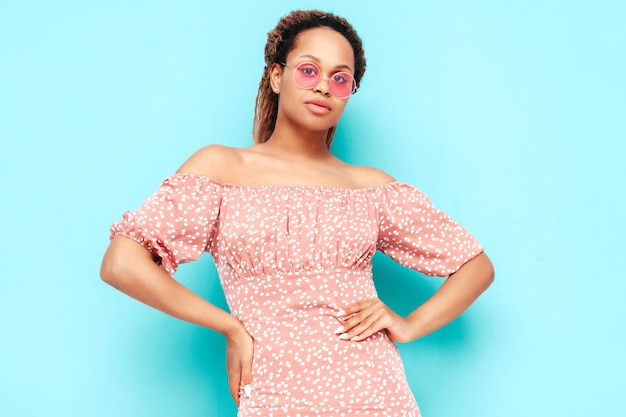 Beautiful black woman with afro curls hairstyle Smiling model dressed in summer dress Sexy carefree female posing near blue wall in studio Tanned and cheerful