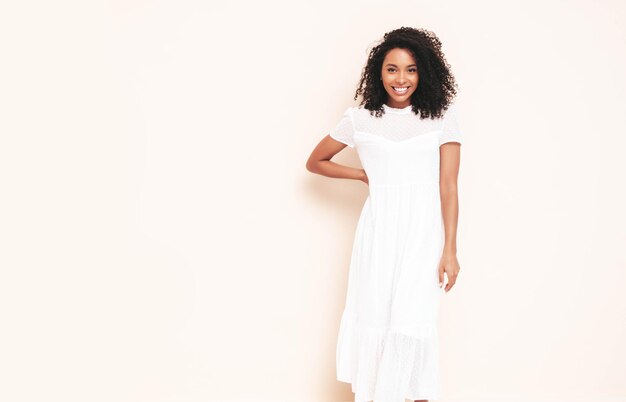 아프리카 컬 헤어스타일을 가진 아름 다운 흑인 여성 흰색 여름 드레스를 입고 웃는 모델 섹시 한 평온한 여성 스튜디오에서 벽 근처 포즈 검게 하 고 쾌활 한 격리