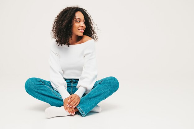 Beautiful black woman with afro curls hairstyle. Smiling model in sweater and trendy jeans clothes