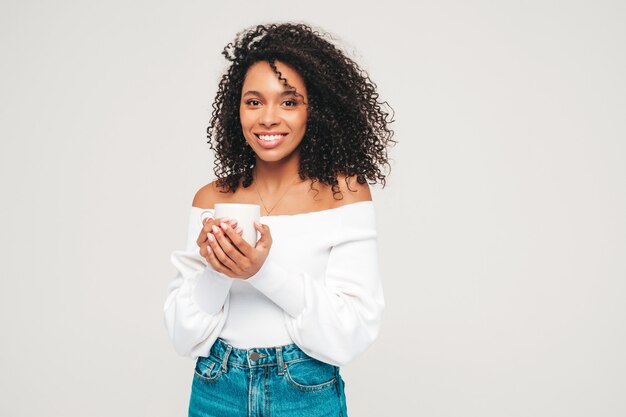 Beautiful black woman with afro curls hairstyle. Smiling model in sweater and trendy jeans clothes. 