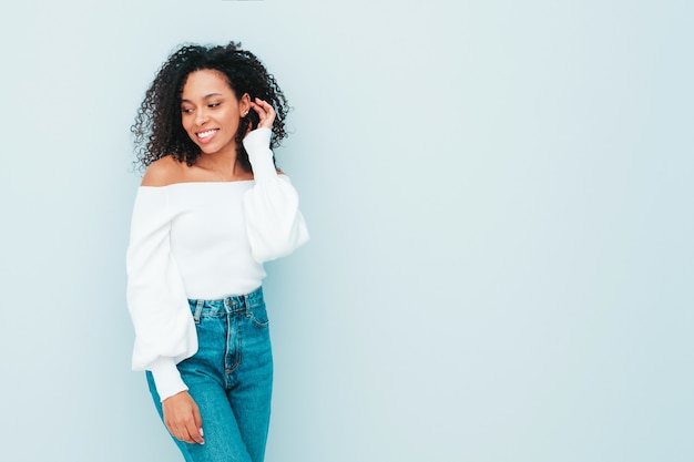 アフロカールの髪型を持つ美しい黒人女性。セーターと流行のジーンズの服を着た笑顔モデル