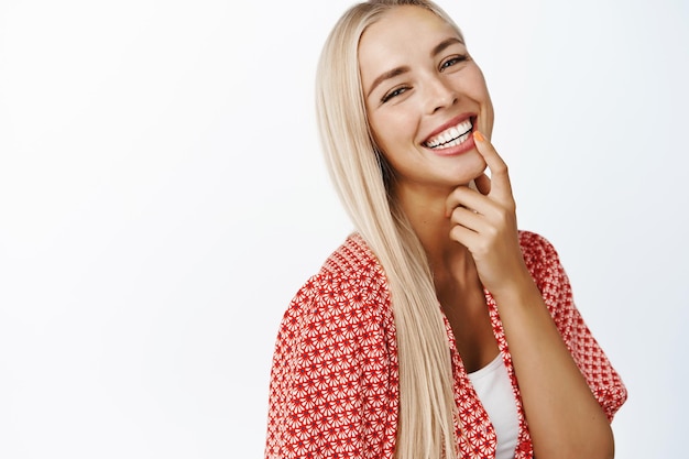 Free photo beautiful blond girl with long healthy hair laughing and smiling at camera standing in summer clothes over white background