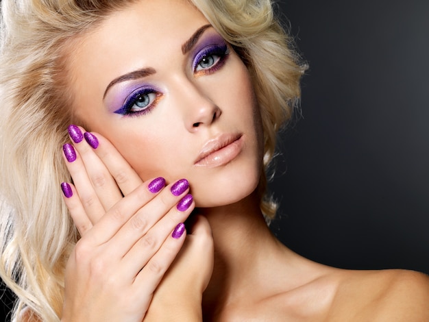 美しい紫色のマニキュアと目のメイクで美しいブロンドの女性