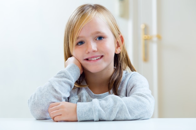 Beautiful blonde child sitting at a table in kitchen.