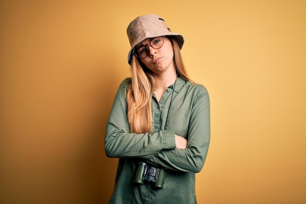 Free photo beautiful blonde explorer woman with blue eyes wearing hat and glasses using binoculars skeptic and nervous disapproving expression on face with crossed arms negative person