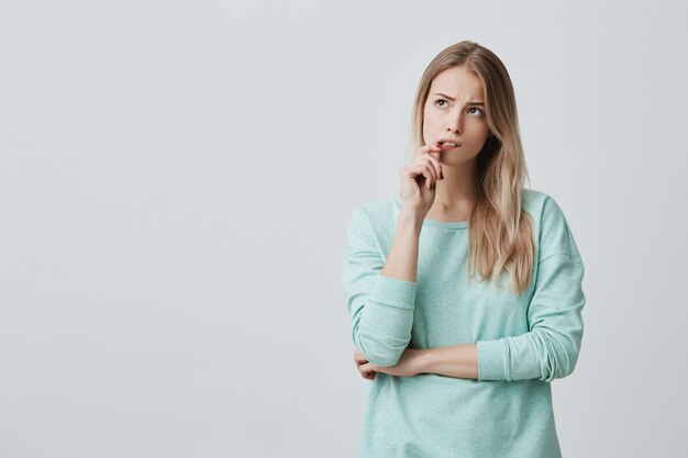 困惑した表情で美しいブロンドの女性は、唇に指を保ち、戸惑うことを避けます