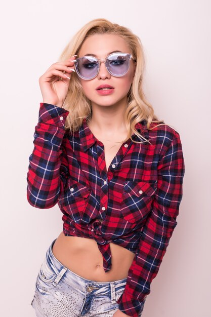 Beautiful blonde girl in red t-shirt and blue sunglasses isolated on pink